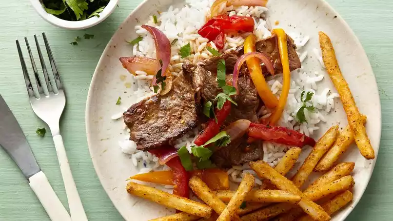 Lomo Saltado Peruano Tradicional con Papas y Arroz Plato de lomo saltado peruano servido con papas fritas doradas y arroz blanco